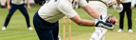 Wicketkeeper diving forward to catch a cricket ball near the stumps